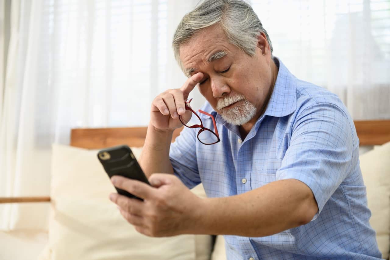 An elderly man struggling to read the words on his phone because of eyesight problems