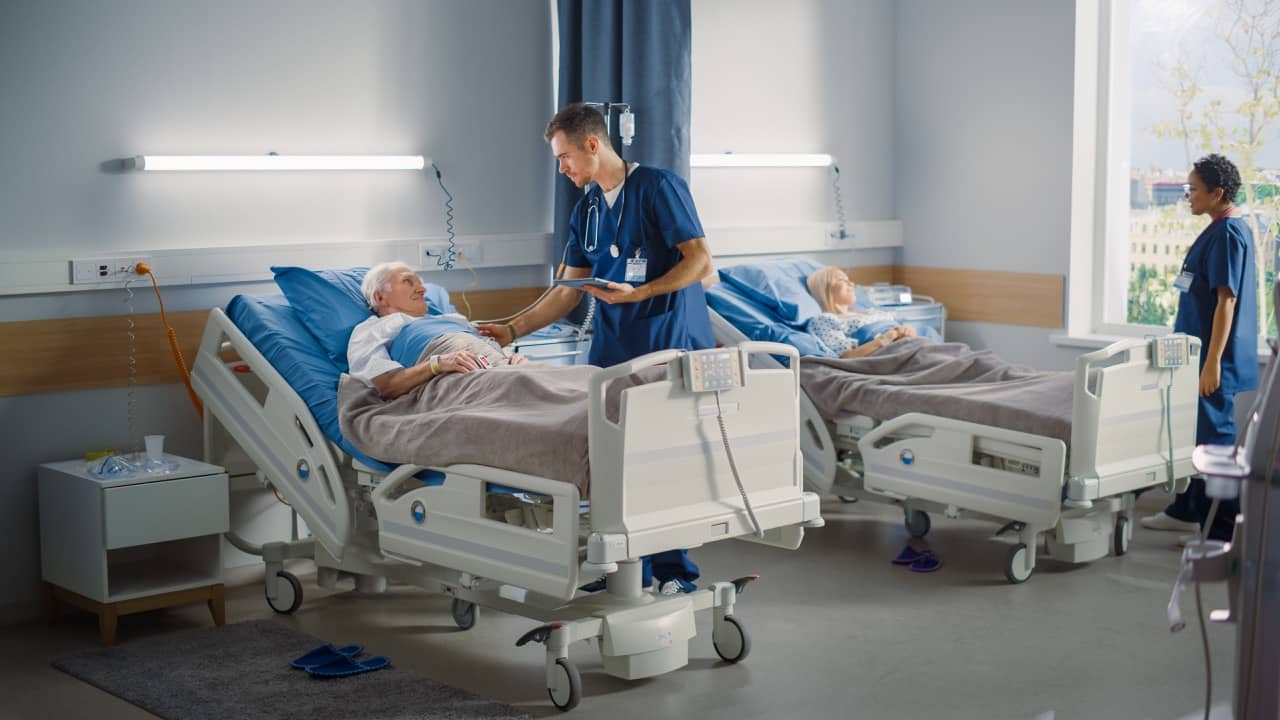 A male nurse talking to an elderly patient in a hospital room
