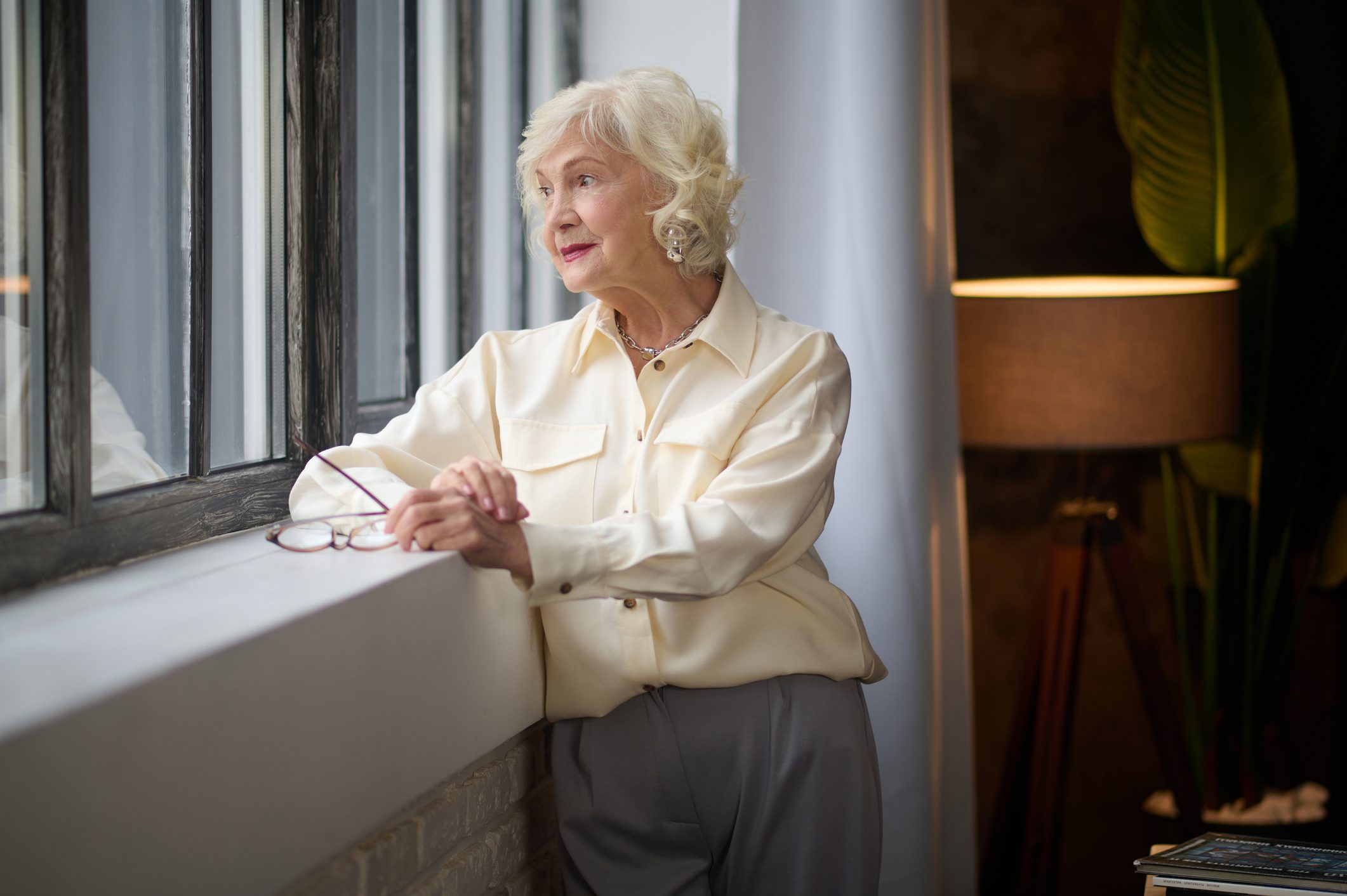 An elderly woman standing by a window.